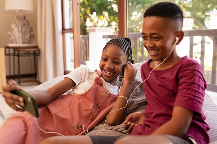 A brother and sister laughing while sharing earphones and a phone