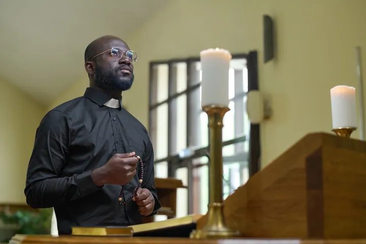 A church leader in a clerical collar holding a rosary